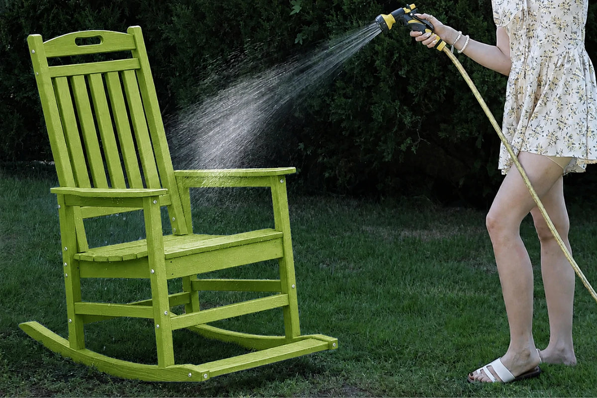 An apple green outdoor rocking chair on a grassy lawn, with a person watering it from a hose in a backyard setting.