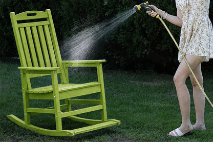 An apple green outdoor rocking chair on a grassy lawn, with a person watering it from a hose in a backyard setting.