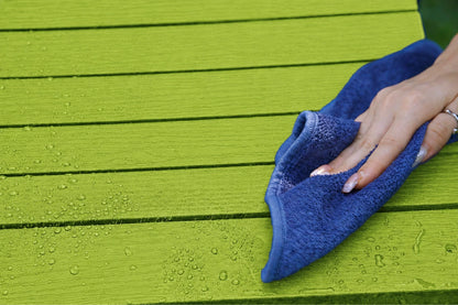 A close-up of a hand wiping an apple green wooden surface with a blue microfiber cloth.