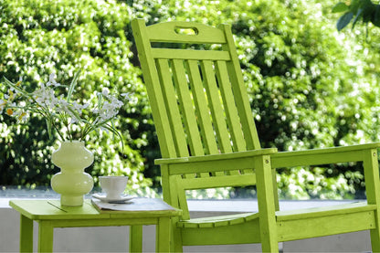 An apple green outdoor wooden chair with a matching side table holding a white vase of flowers and a white cup, set against a blurred green garden background.