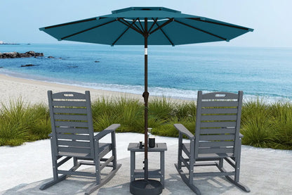 Two gray chairs with a small table and teal umbrella on a sandy beach.