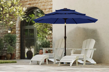 Blue patio umbrella over white Adirondack chairs on a patio with stone wall and greenery in the background.
