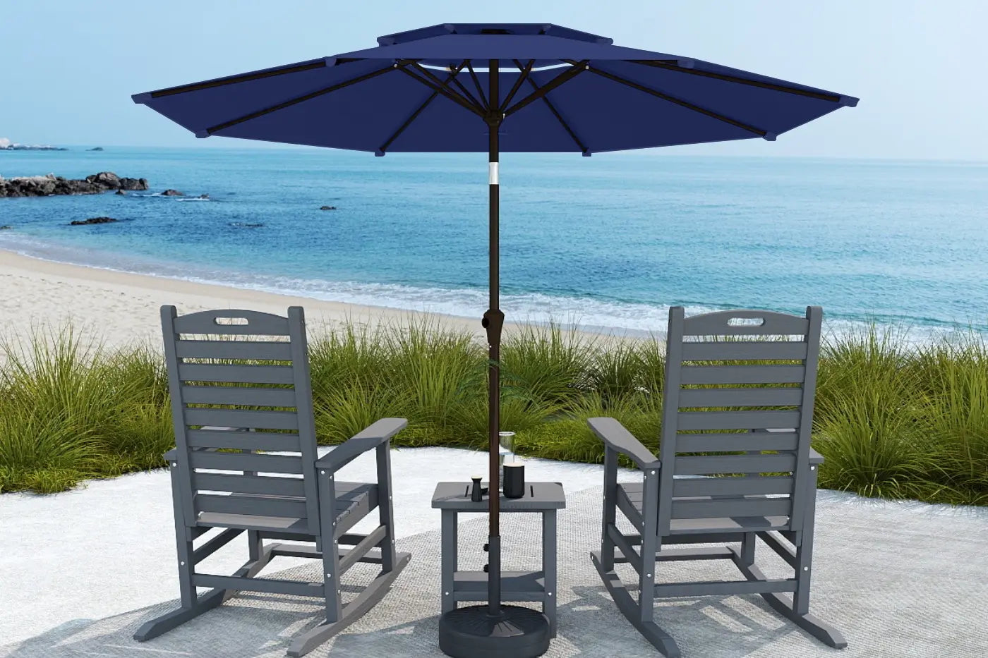 Two gray chairs with a small table and blue umbrella on a sandy beach.