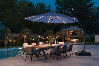 Outdoor dining setup with a large umbrella over a table by a pool at night.
