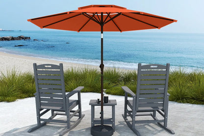 Outdoor patio set with two gray chairs, a small table, and an orange umbrella on a sandy beach.
