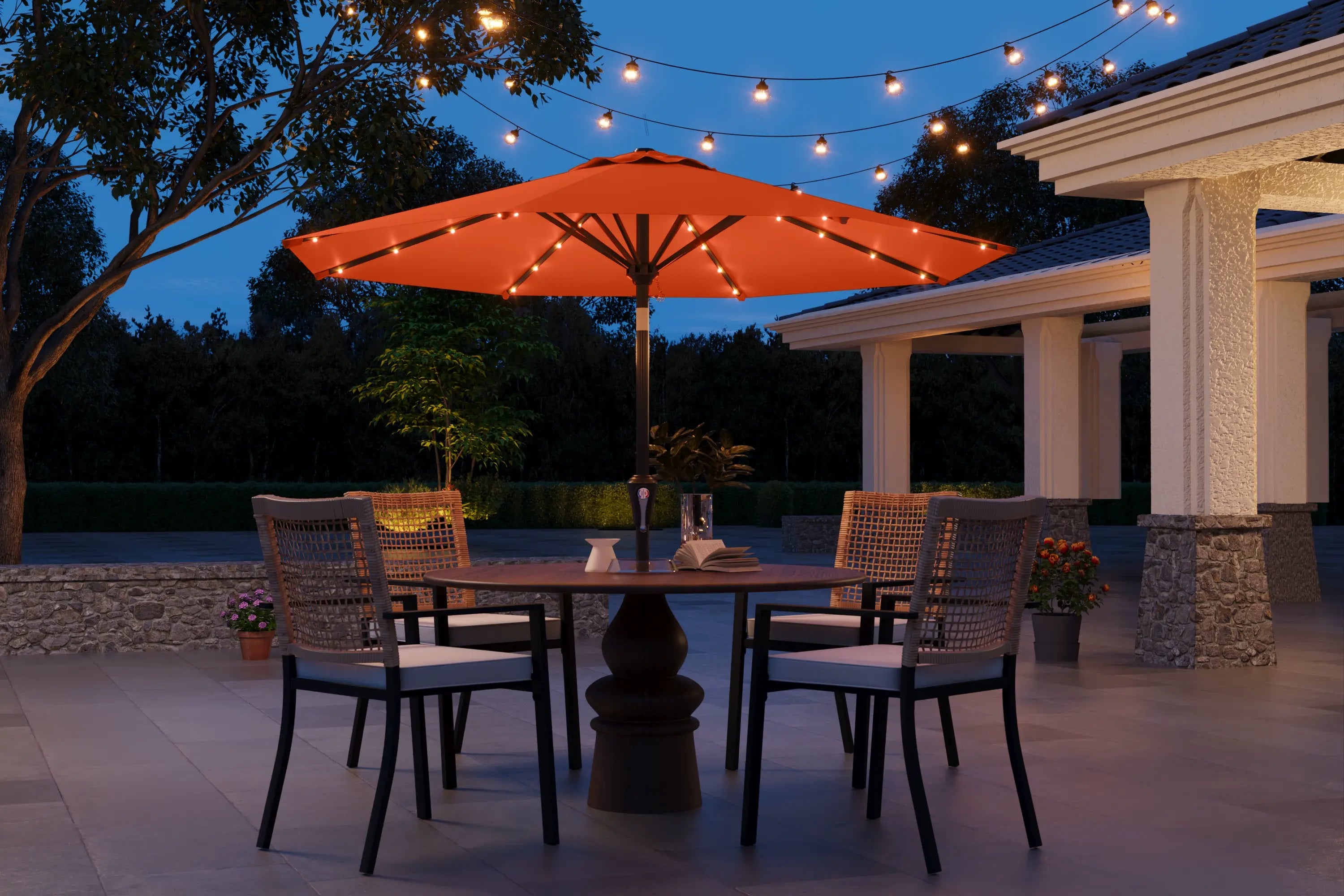 Outdoor patio setting with a table, chairs, and string lights under an umbrella at dusk.