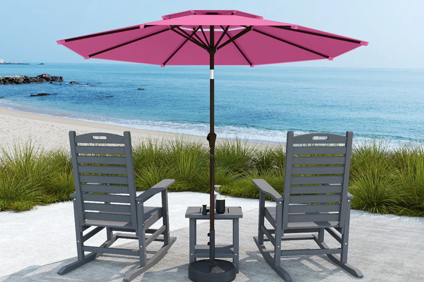 Two gray chairs with a pink umbrella on a sandy area near the ocean.