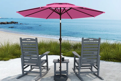 Two gray chairs with a pink umbrella on a sandy area near the ocean.