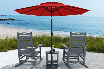 Red patio umbrella with two gray chairs and a small table on a sandy beach.
