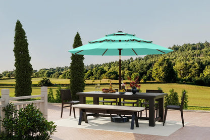 Outdoor dining set with a large green umbrella on a patio, surrounded by trees and fields.