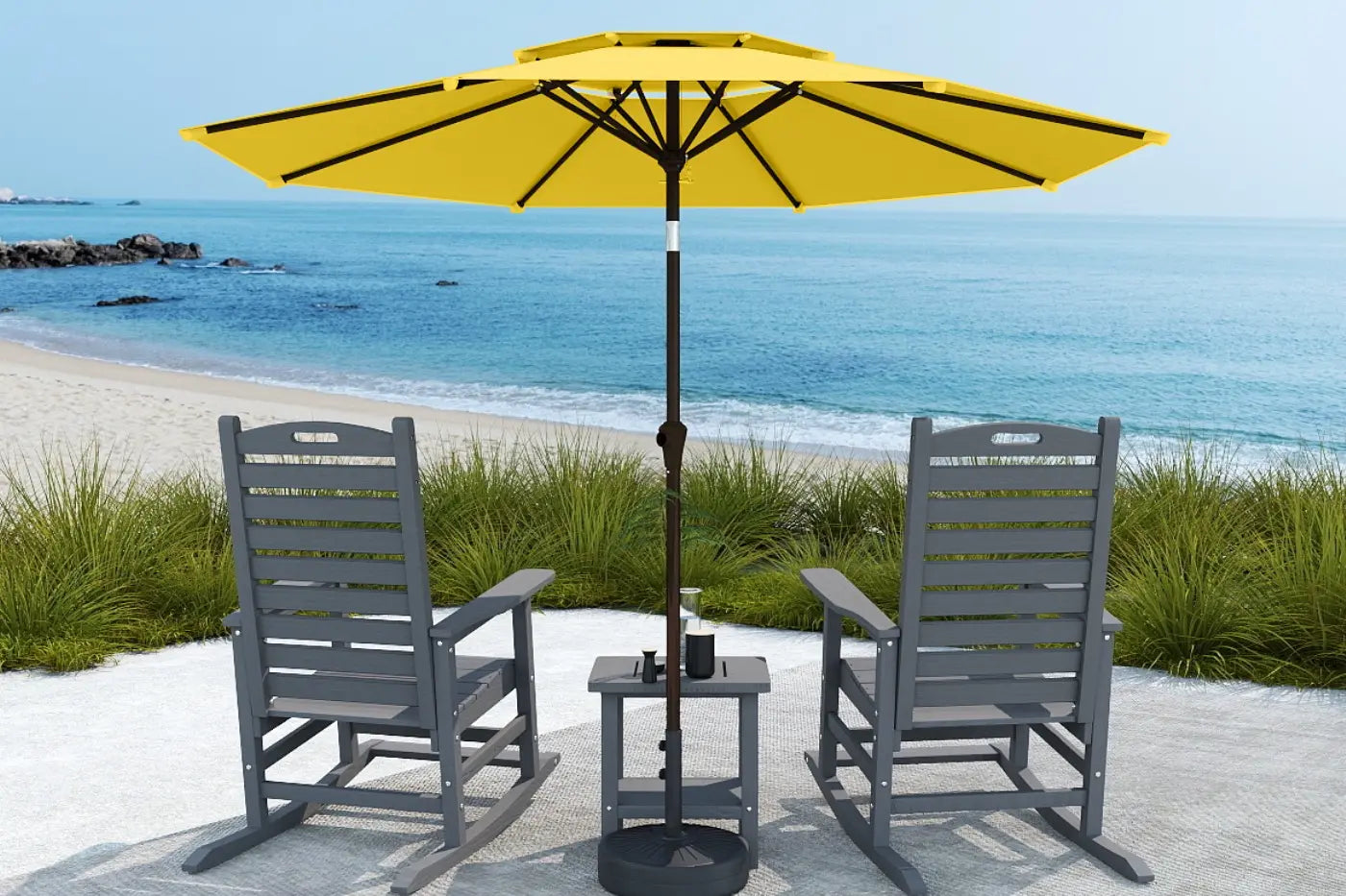 Two gray chairs with a yellow umbrella on a sandy area near the beach.