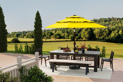 Outdoor patio set with a yellow umbrella, table, chairs, and a fire pit on a deck with a scenic background.