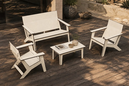 A beige four-piece outdoor patio furniture set including a loveseat, two armchairs, and a small coffee table arranged on a dark wood deck.