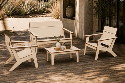 A four-piece outdoor patio furniture set  including a loveseat, two armchairs, and a small coffee table, arranged on a wooden deck in a sunny patio setting.