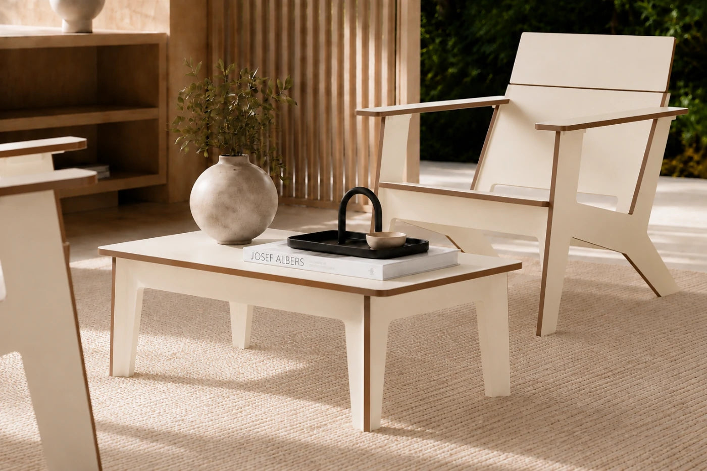 A modern outdoor chair with a low rectangular coffee table, styled in a warm, sunlit patio setting with a textured rug, wooden slat screen, and decorative ceramic vase.