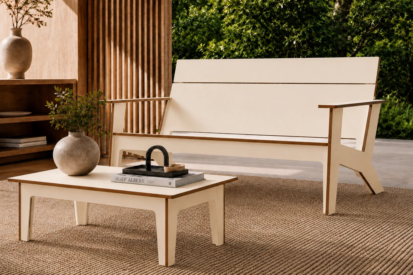 A modern outdoor loveseat with a beige fabric seat and backrest, paired with a matching low-profile coffee table, set on a woven rug in a patio environment.