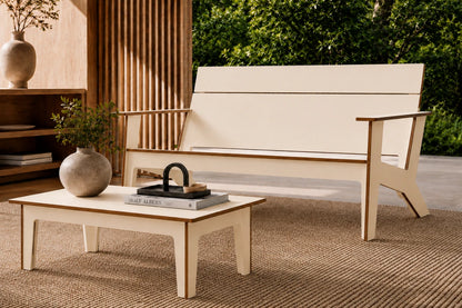 A modern outdoor loveseat with a beige fabric seat and backrest, paired with a matching low-profile coffee table, set on a woven rug in a patio environment.