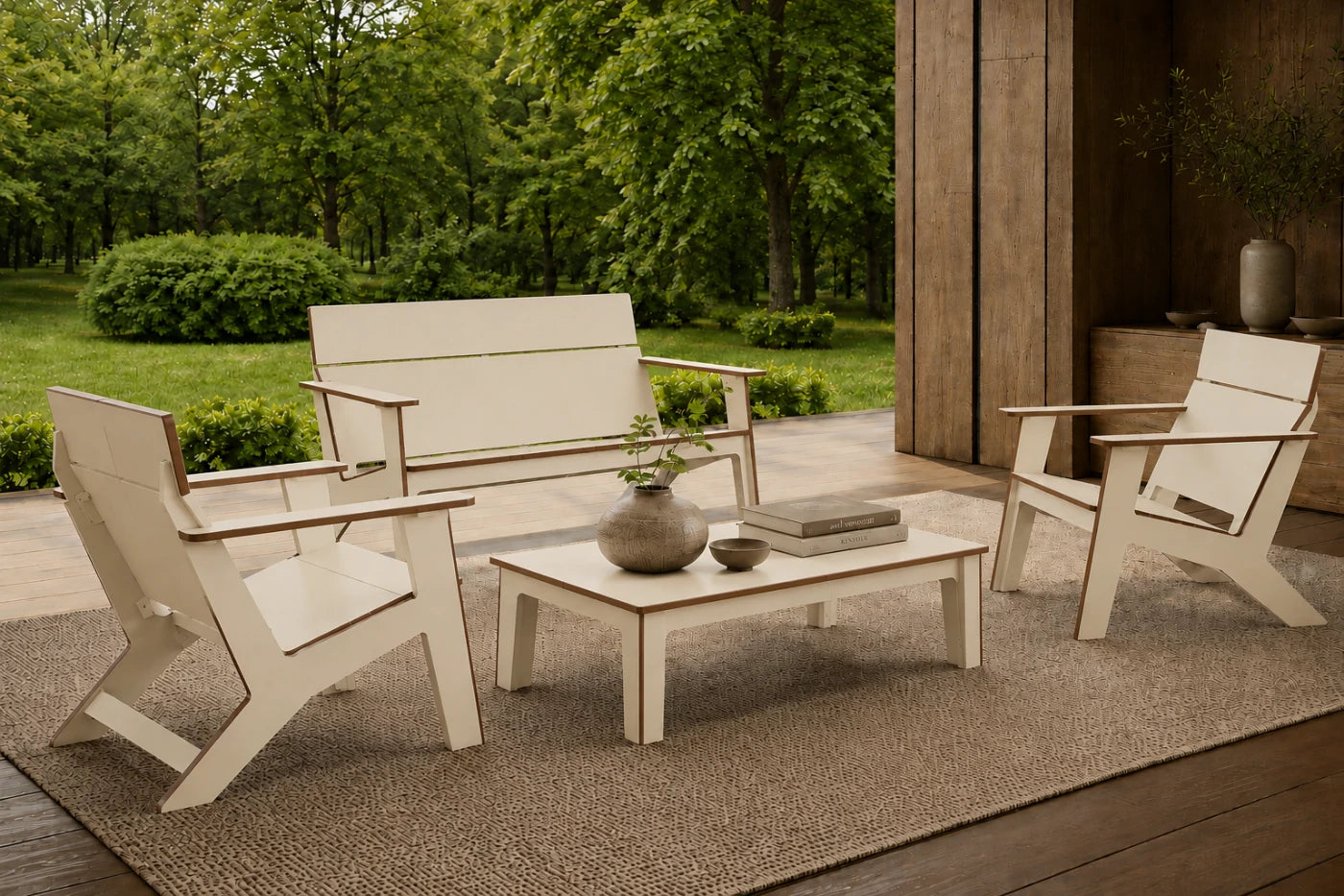 A beige 4-piece outdoor patio conversation set including a loveseat, two armchairs, and a coffee table arranged on a woven rug in a garden setting.
