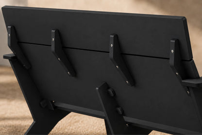 Close-up of the back of a black outdoor chair shown against a blurred beige background.