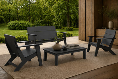 A 4-piece outdoor patio furniture set in black, including a loveseat, two armchairs, and a rectangular coffee table, arranged on a jute rug in a patio setting with a green garden background.