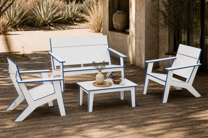 A four-piece outdoor patio furniture set with a loveseat, two armchairs, and a small coffee table. The furniture is white with a distinctive blue trim outline, arranged on a wooden deck in front of a stucco wall.