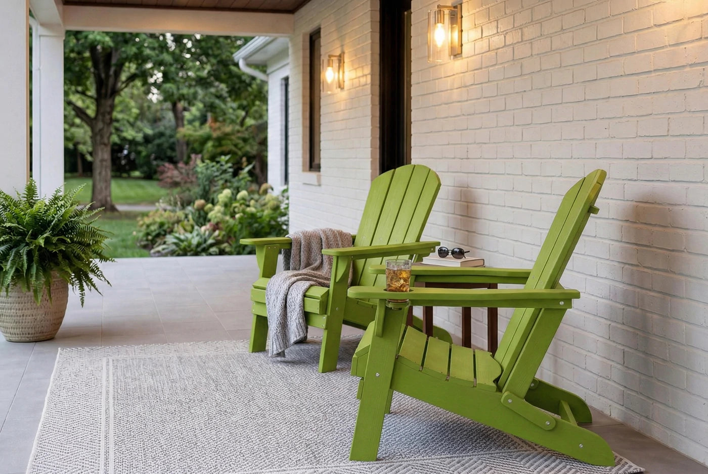 Two green Adirondack chairs on a porch with a white brick wall and outdoor setting.