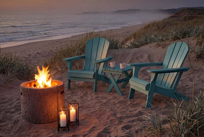 Two Adirondack chairs by a fire pit on a sandy beach at dusk.