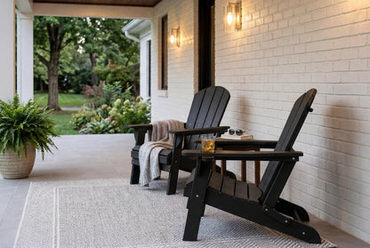 Two black Adirondack chairs on a porch with a white brick wall and outdoor plants.