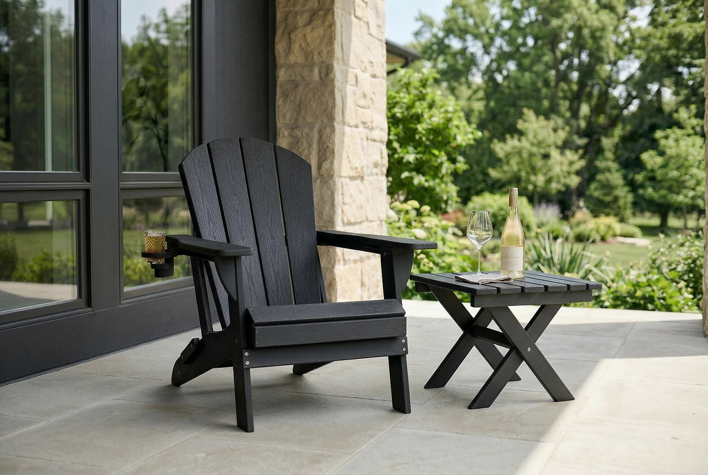 Black Adirondack chair on a patio with a small table and wine bottle.