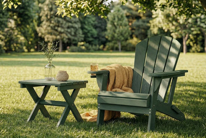 Green Adirondack chair with a blanket and small table on grass with trees in the background