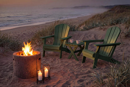 Two green Adirondack chairs around a fire pit on a sandy beach at dusk.