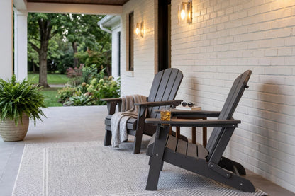 Two Adirondack chairs on a porch with a white brick wall and outdoor setting.