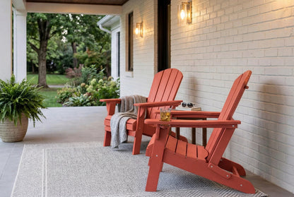 Two red Adirondack chairs on a porch with a small table and plants.