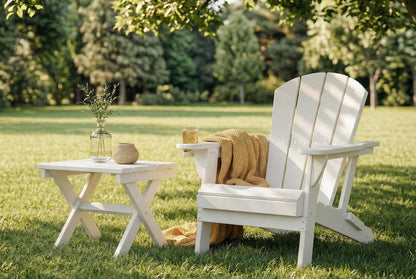 White Adirondack chair with a small table and a drink on a grassy lawn with trees in the background