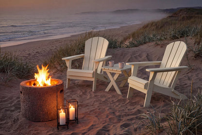 Two Adirondack chairs by a fire pit on a sandy beach with ocean view.