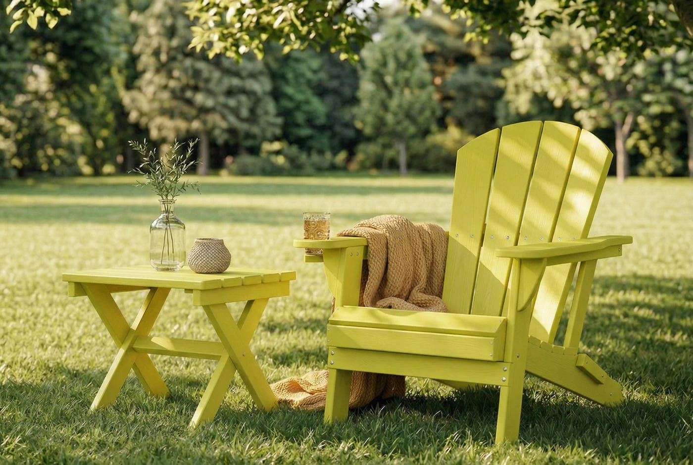 Yellow Adirondack chair and table set on a grassy lawn with a blanket and small items.