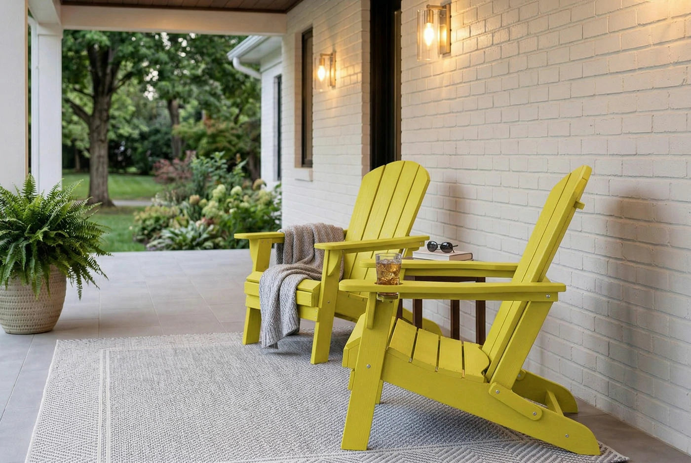 Two yellow Adirondack chairs on a porch with a white brick wall and outdoor plants.