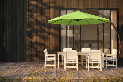 An apple green patio umbrella with a curved dark metal arm stands over a white outdoor dining table and chairs on a wooden deck in front of a modern house with dark wood siding.