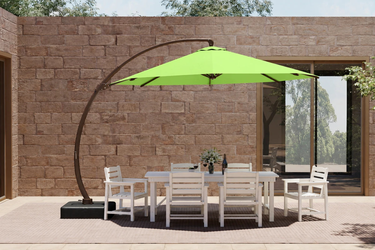 A large outdoor patio setup featuring an apple green cantilever umbrella over a white dining table and six matching chairs, set against a stone wall background.