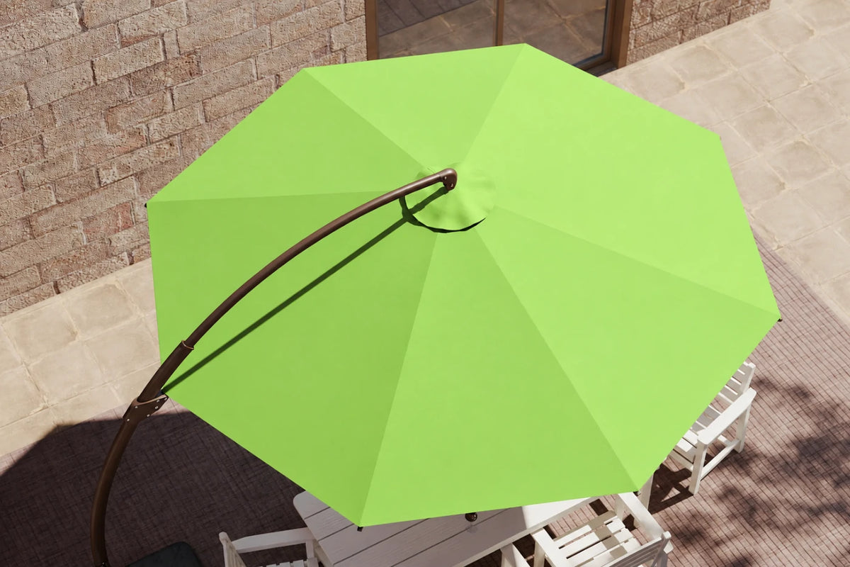 Apple pink patio umbrella with a curved black metal pole, shown from an overhead angle in an outdoor patio setting with white chairs and a stone wall background.