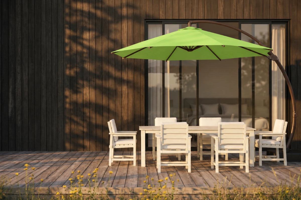 A modern outdoor patio setup featuring a cantilever umbrella, a white rectangular dining table, and six matching white lounge chairs, set against a dark wood-paneled house facade.