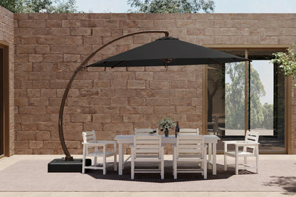 A large outdoor patio setup featuring a black cantilever umbrella over a white dining table and six matching chairs, set against a stone wall background.