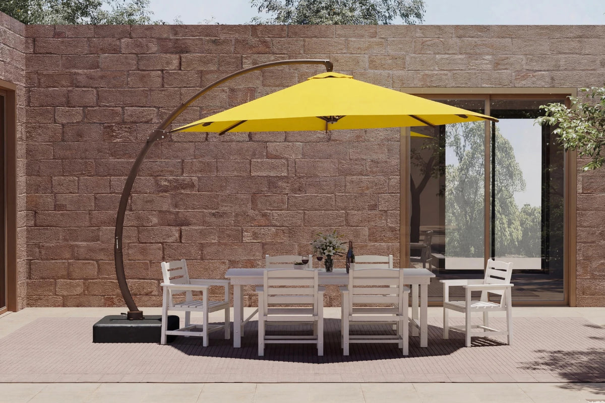 A large yellow cantilever patio umbrella with a curved black metal arm stands over a white outdoor dining table and six matching chairs, set against a brown stone wall.