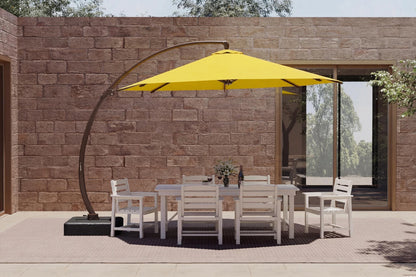A large yellow cantilever patio umbrella with a curved black metal arm stands over a white outdoor dining table and six matching chairs, set against a brown stone wall.