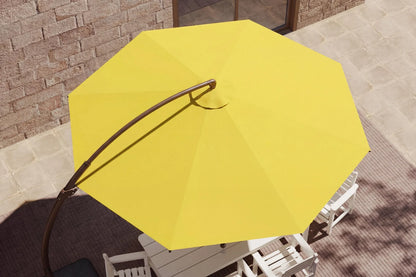 Yellow patio umbrella with a curved black metal pole, shown from an overhead angle in an outdoor patio setting with white chairs and a stone wall background.