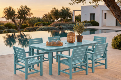 An Aruba blue outdoor dining set consisting of a rectangular slatted table and six matching armchairs, arranged on a stone patio next to an infinity pool at sunset.