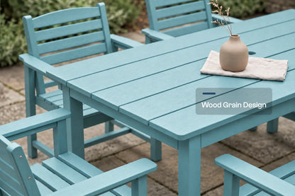 An Aruba blue outdoor dining set featuring a slatted rectangular table and matching armchairs on a stone patio, with a small beige vase on the table. A text overlay reads 'Wood Grain Design'.