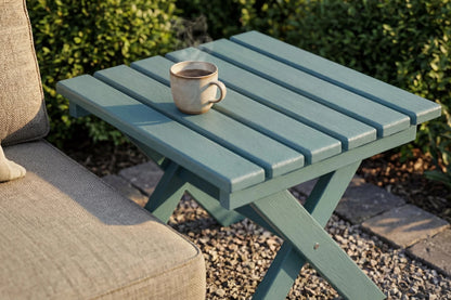 Teal outdoor side table with a cup on it, next to a beige cushioned chair.