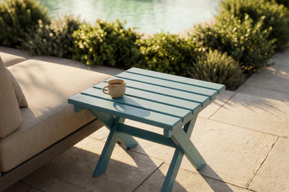 HDPE side table with a cup on it next to a beige outdoor sofa by a pool.
