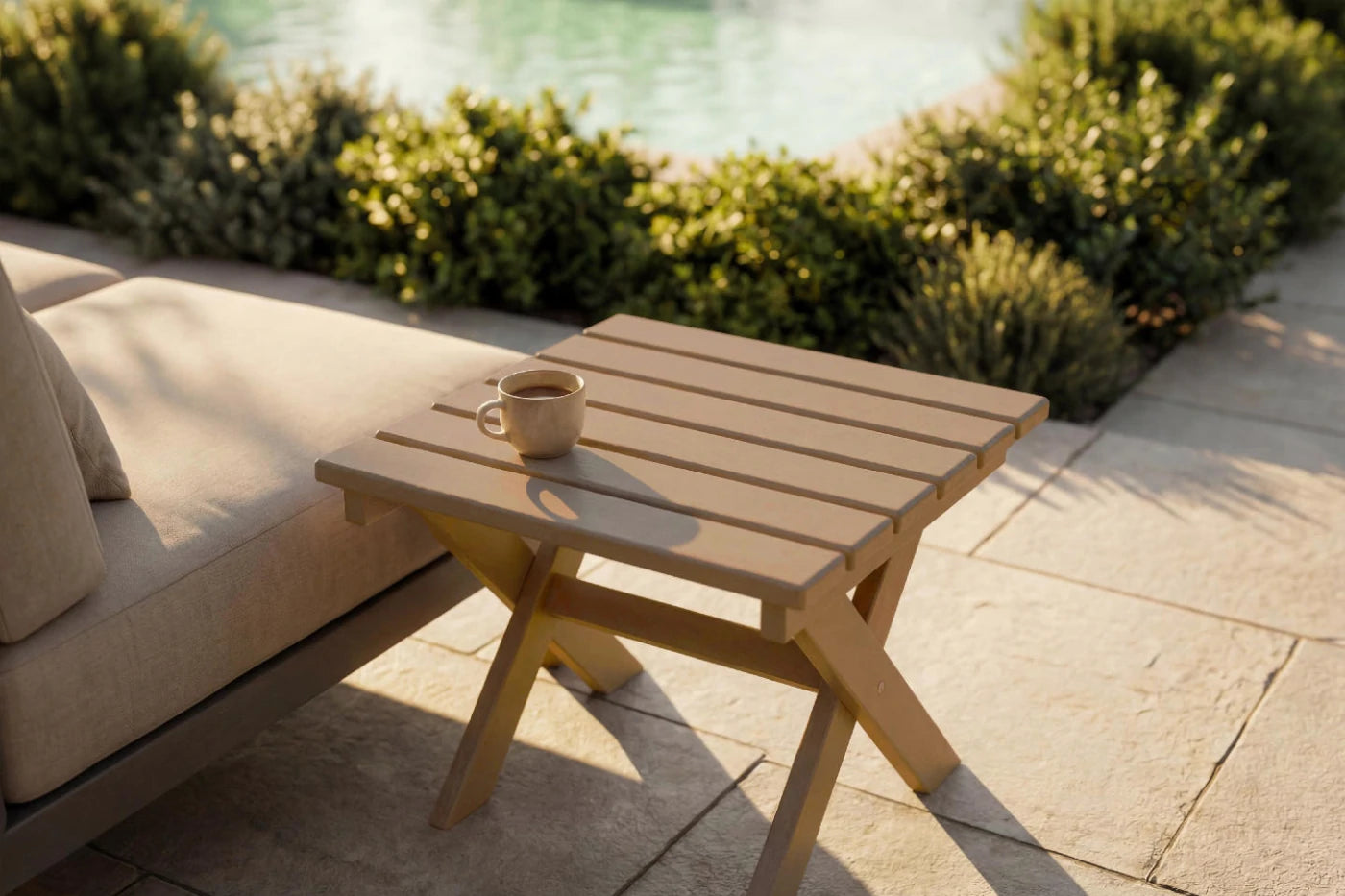 HDPE side table with a cup on it next to a beige outdoor sofa by a poolside.